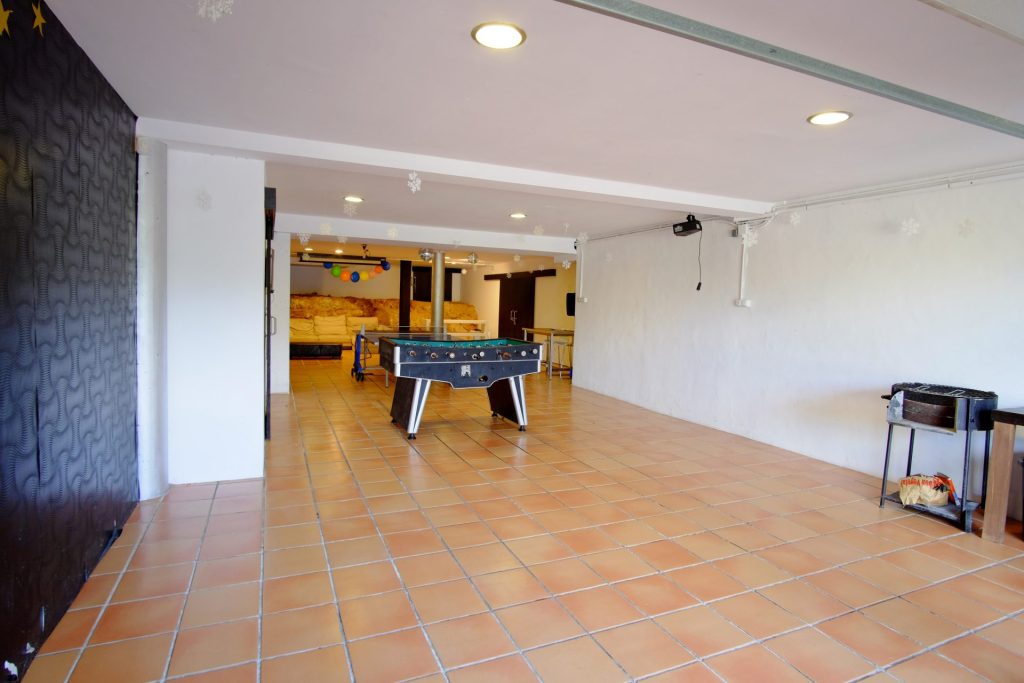 Una amplia sala de juegos con futbolín sobre suelo de baldosas, paredes blancas y luces de techo. La habitación tiene un ambiente acogedor y agradable.